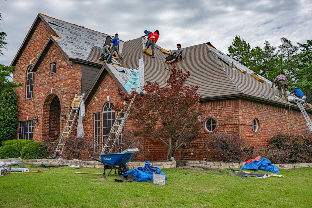 Roofers working on brick home in Allen, Texas, addressing shingles and roofing materials.